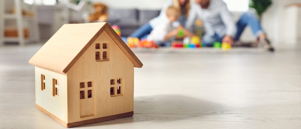 柏市で信頼できる不動産会社を選ぶイメージとして、家族が床に座って木製の家の模型で遊んでいる様子。地域密着型と大手仲介会社の違いや、ファミリー層向け物件選びのポイントを伝えるための写真。