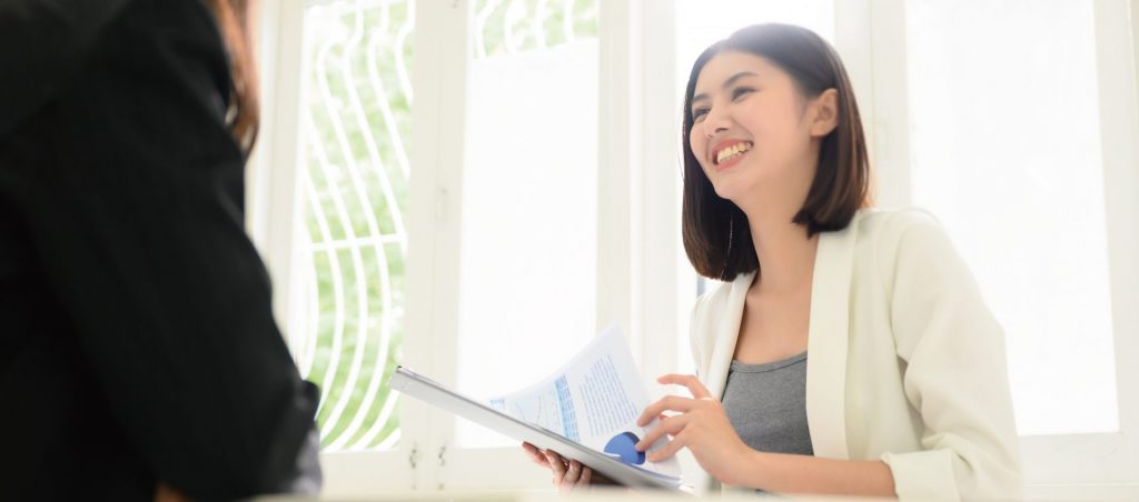 笑顔で書類を持つ女性と話す面接官。不動産業界のアルバイト求人に応募するシーンのイメージ