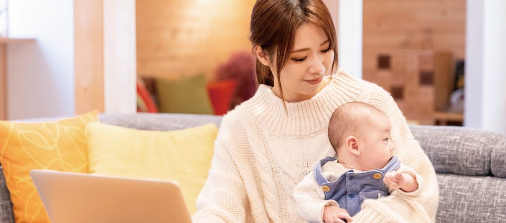 赤ちゃんを抱えながらノートパソコンを使う女性の姿。柏市での不動産管理会社の求人や働き方に関するよくある質問を想起させる場面。