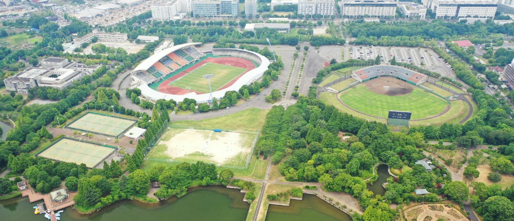 柏市の自然豊かな公園と大きなスタジアム、住宅地が広がる風景。都心からのアクセスが良く、緑や水辺など自然環境も充実している柏エリアの住みやすさや子育て環境の魅力がわかるイメージ