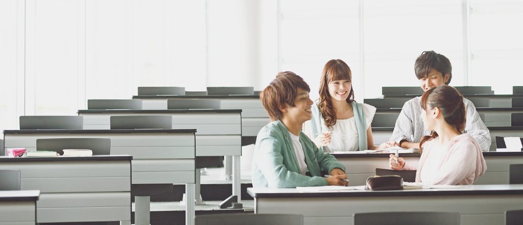 大学の講義室で談笑する4人の学生。我孫子・柏エリアから大学への通学の便利さと安全性を示すイメージ
