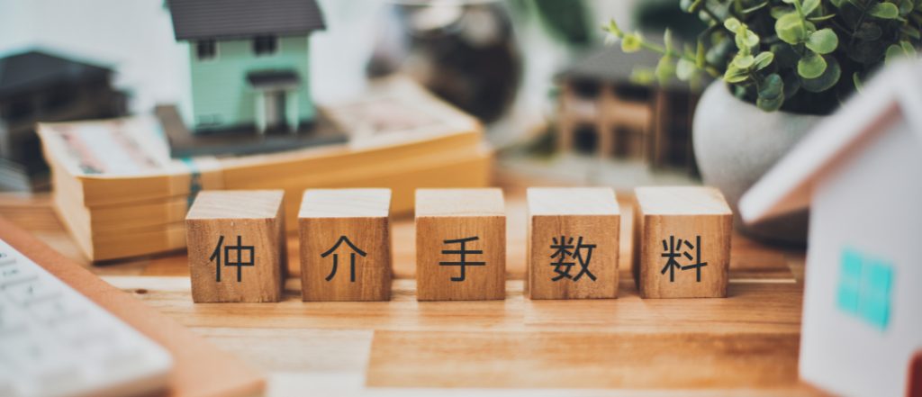 「仲介手数料」と書かれた木製ブロックとミニチュアの家。不動産売買における仲介手数料の仕組みと費用を象徴するイメージ。