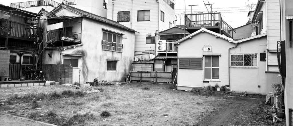 雑草が生い茂り、外壁が古びた、手入れされていない空き家の一軒家。空き家を放置することによるリスクや荒廃を表現するモノクロ写真。

